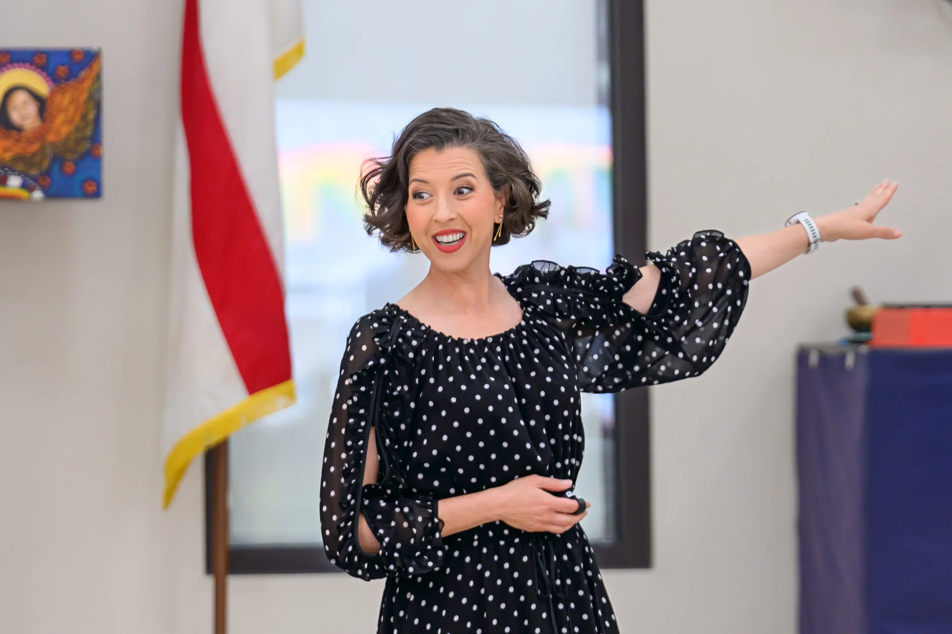 Lisette mid-gesture during a vocal demonstration, one arm extended, the Louisiana state flag visible behind her.